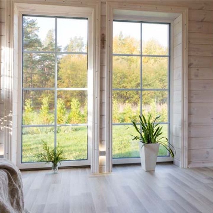 Bright living room with large windows, light wood walls, and potted plants overlooking greenery outside