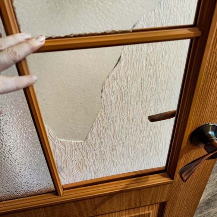 Wooden door with a cracked glass panel and a hand holding the frame