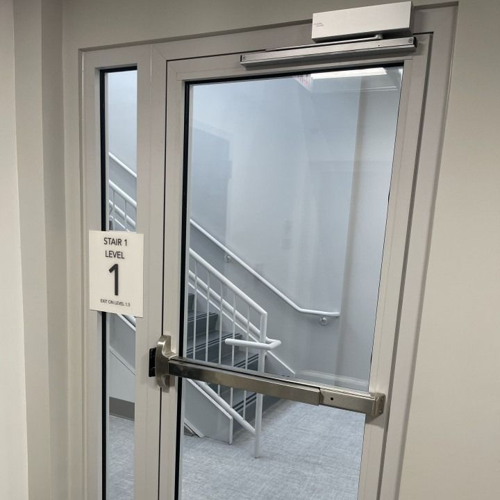 Glass door entrance to a stairwell with gray stairs and a handrail inside