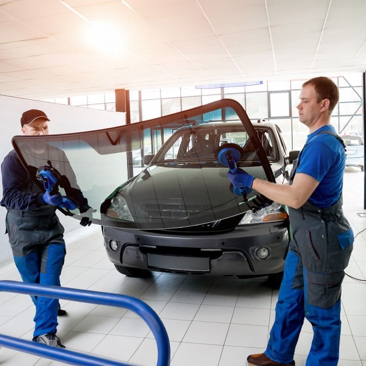 Two auto technicians install a windshield on a car in a bright repair shop.
