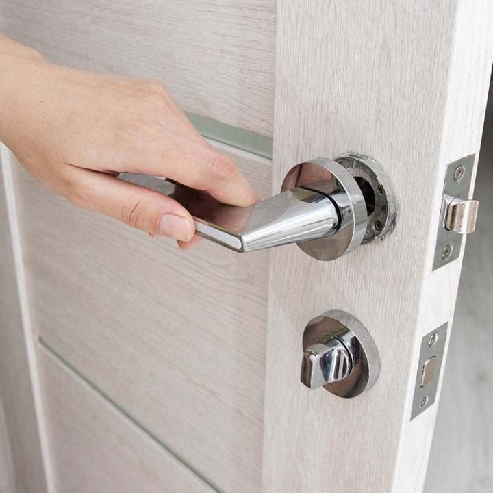 Hand turning a silver door handle on a white interior door