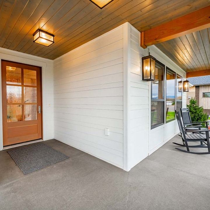 Covered front porch with orange door, white siding, wood ceiling, and rocking chairs