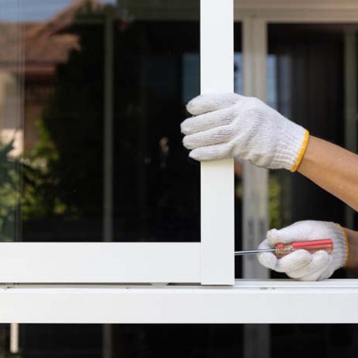 Gloved hands adjusting a white window frame with a red tool