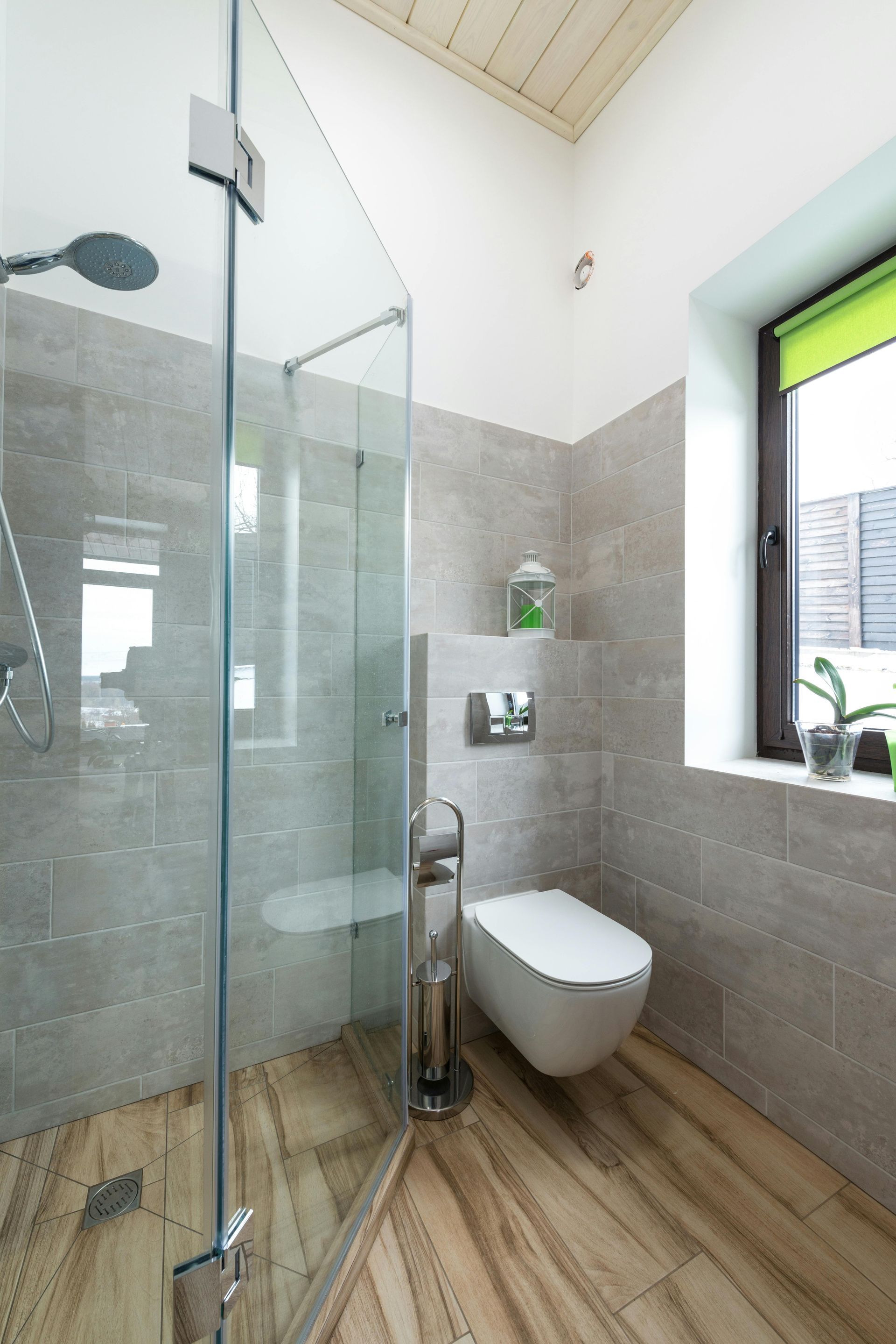 Modern bathroom with glass shower, wall-mounted toilet, gray tiles, and wood-look floor