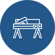 A blue circle with a line drawing of a wooden table with a saw on it.