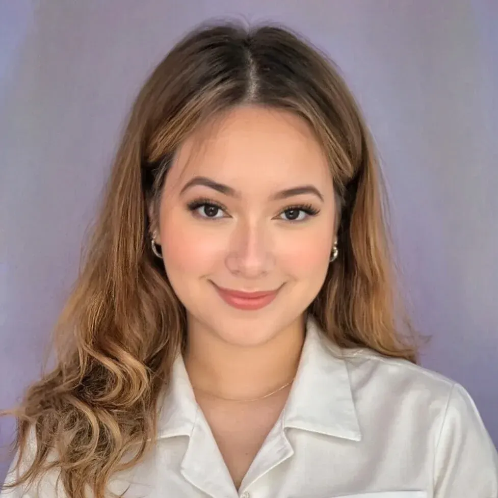 Studio portrait of a smiling woman in a white blouse with wavy hair on a soft purple background
