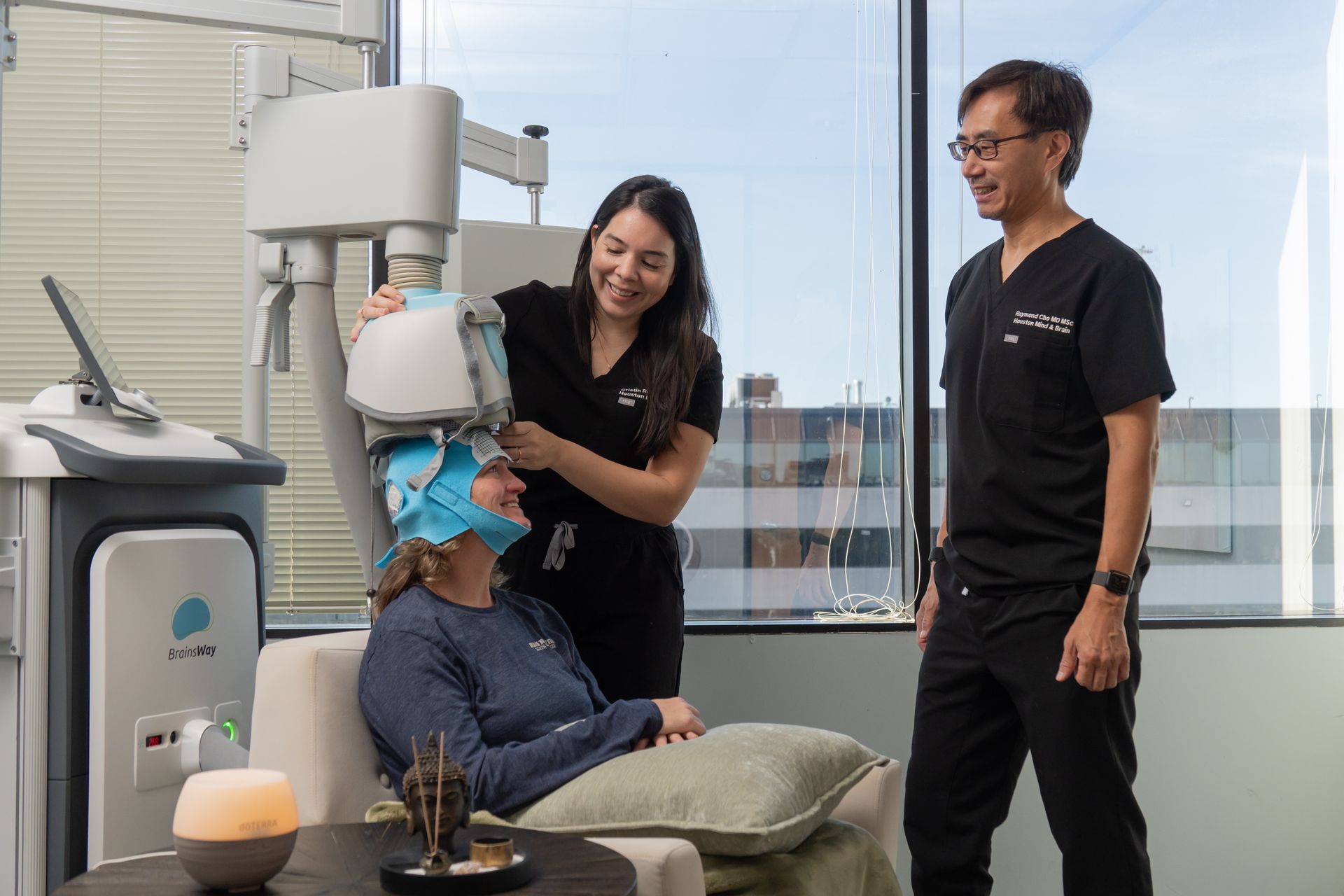 Woman receiving a facial treatment while two clinicians stand nearby in a bright spa clinic room