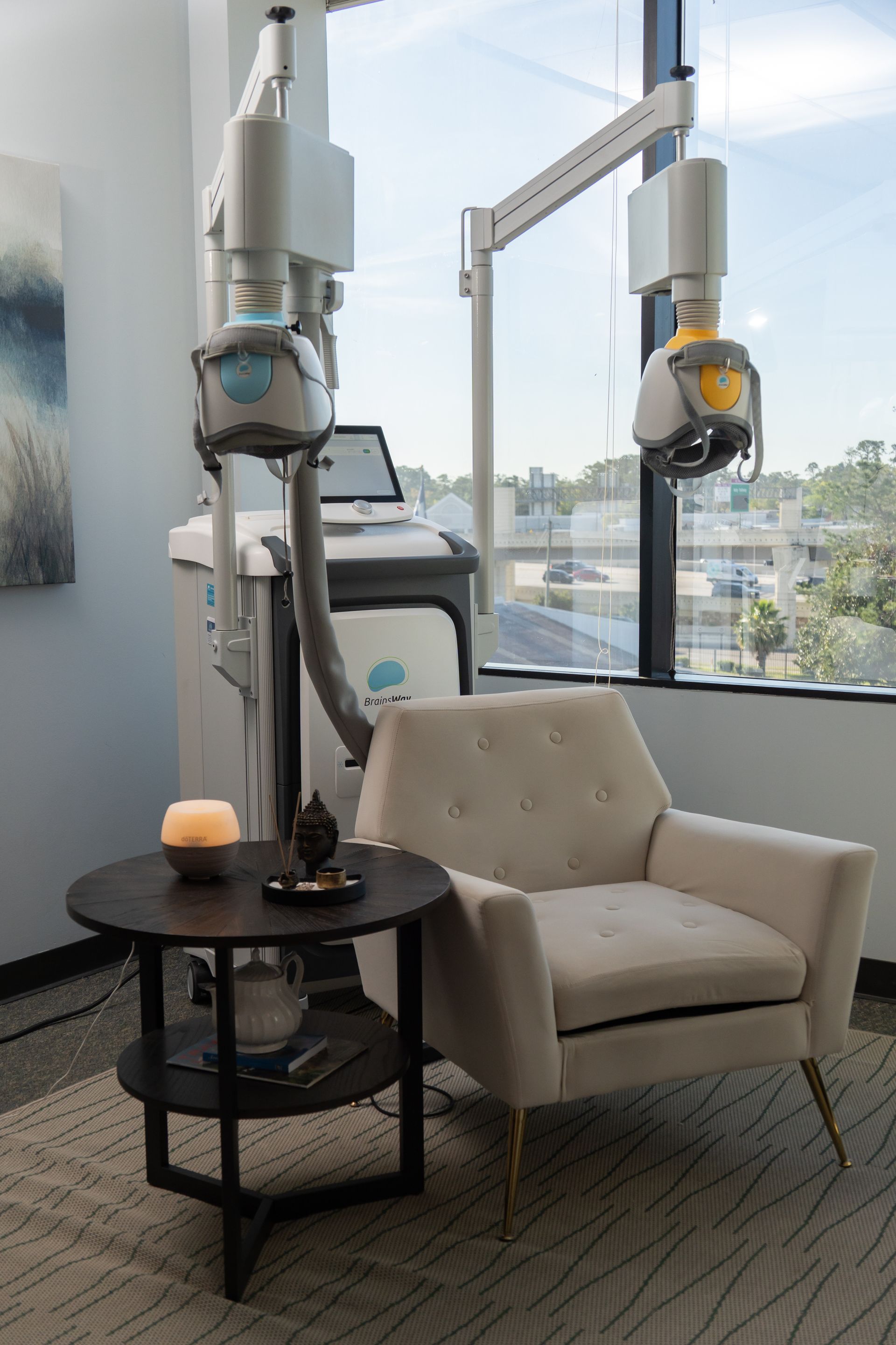 Modern treatment room with two dental X-ray machines, beige armchair, and round side table by a window.