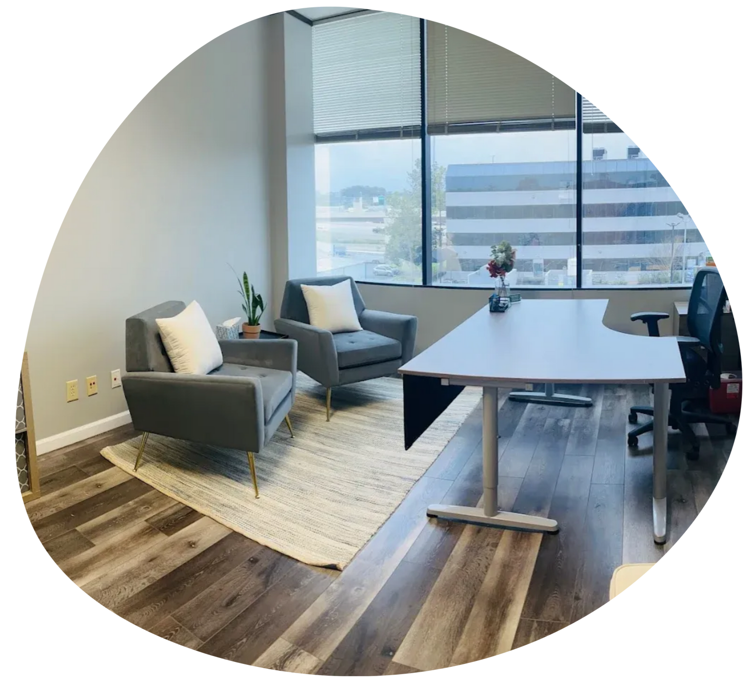 Modern office lounge with gray chairs, a table, and large windows overlooking city buildings