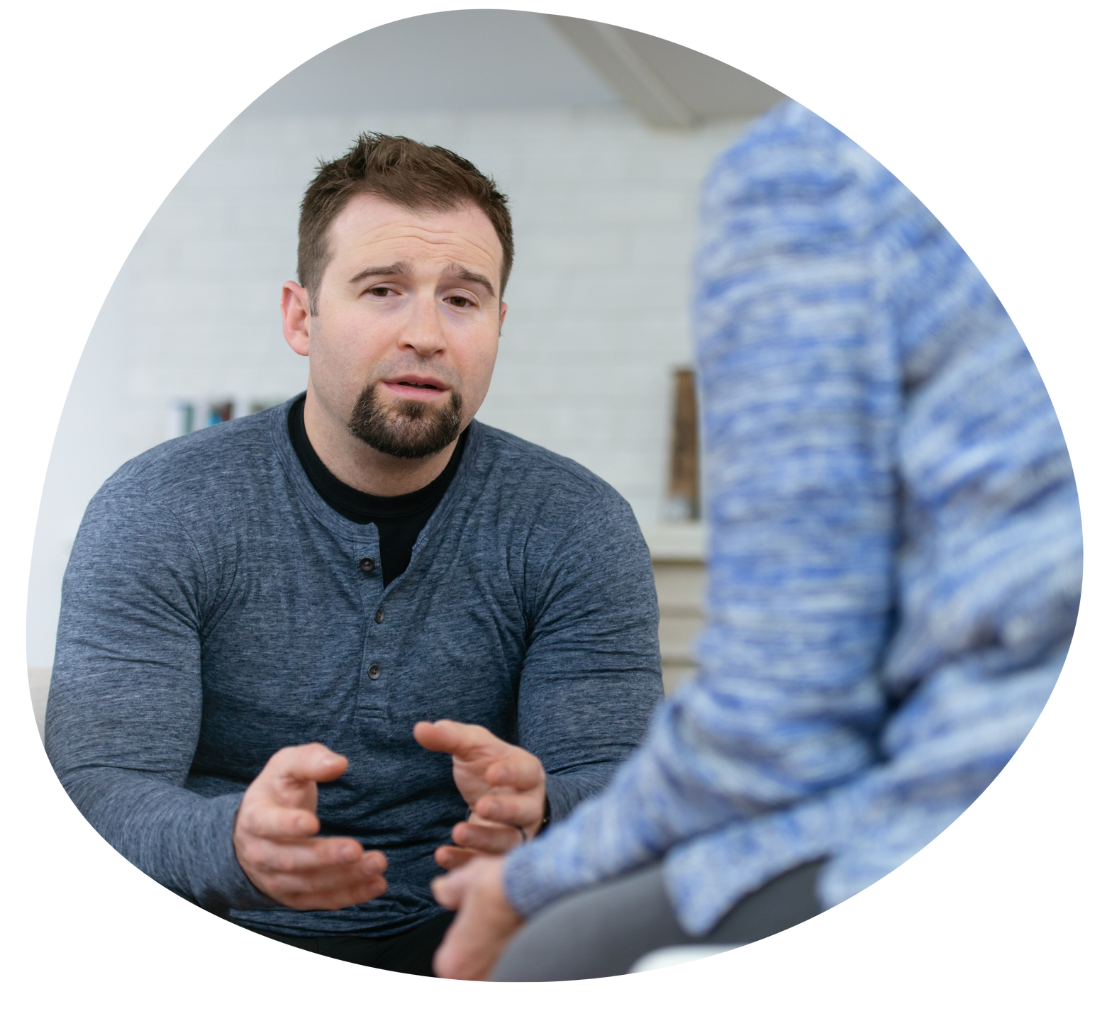 Man speaking in a gray sweater during an outdoor conversation with another person in a blue sweater