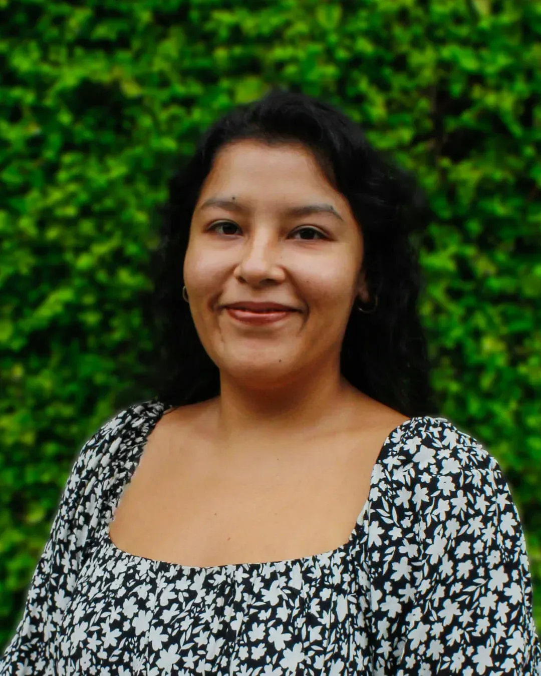 Woman smiling in a black-and-white floral top against a green leafy background