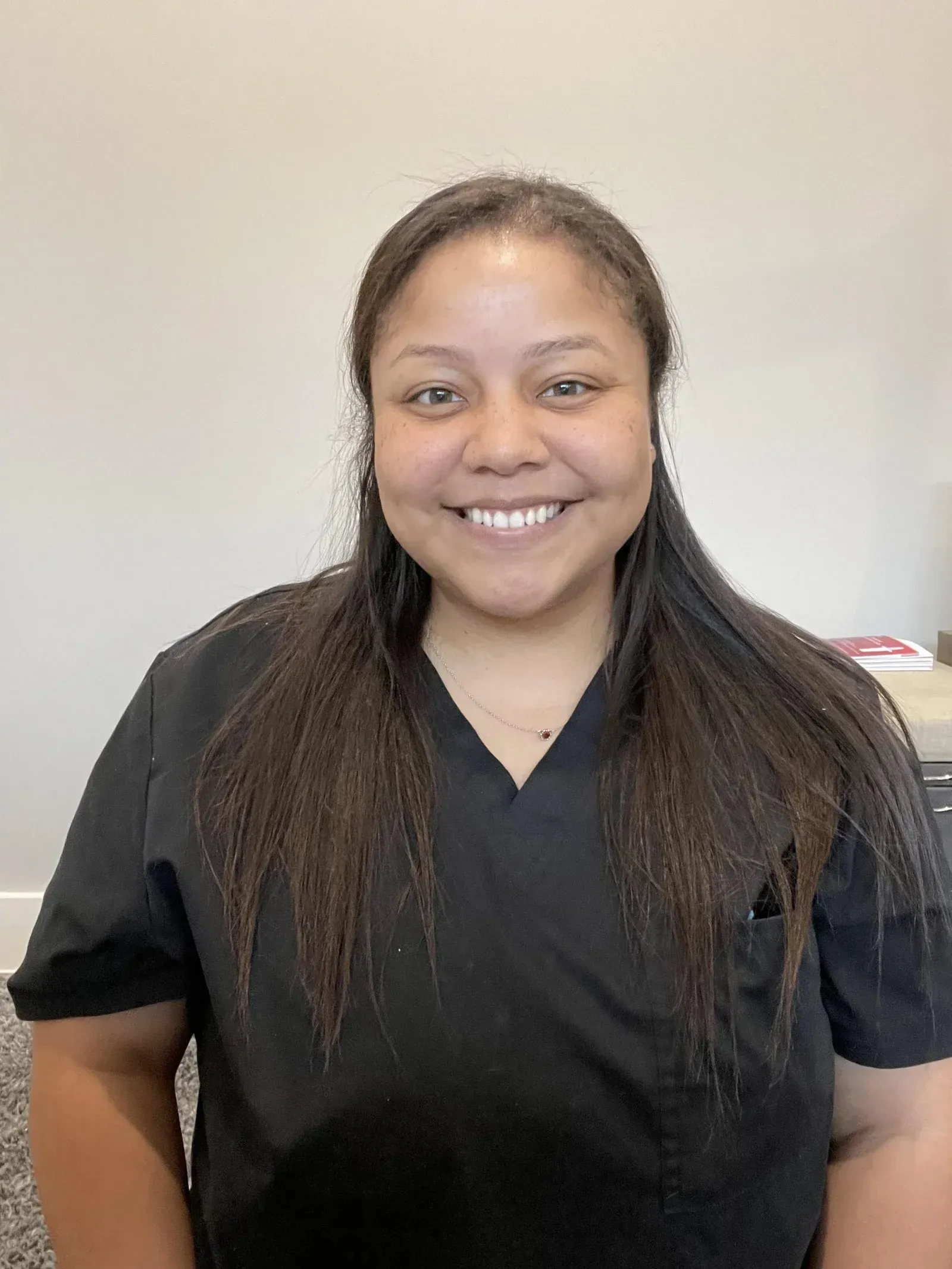 Smiling person in black scrubs standing against a plain light background.