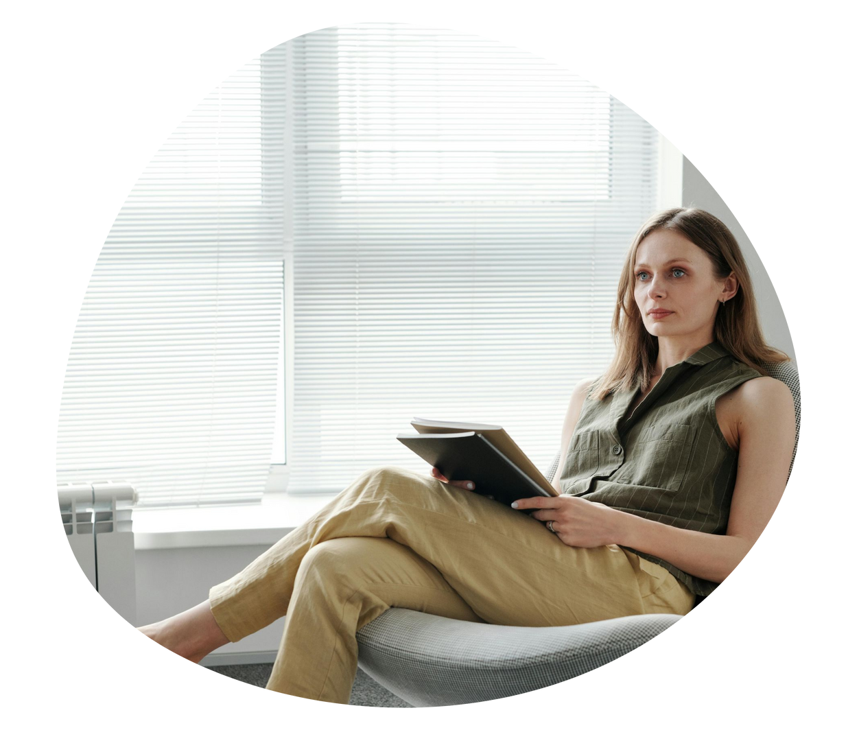 Person sitting on a sofa by a bright window, holding a tablet and looking at the camera.