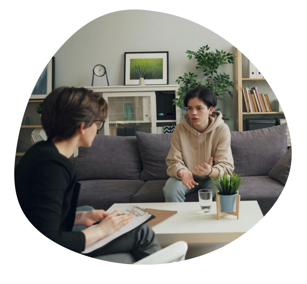 Two people in a living room having a conversation across a coffee table with a notebook and plant.
