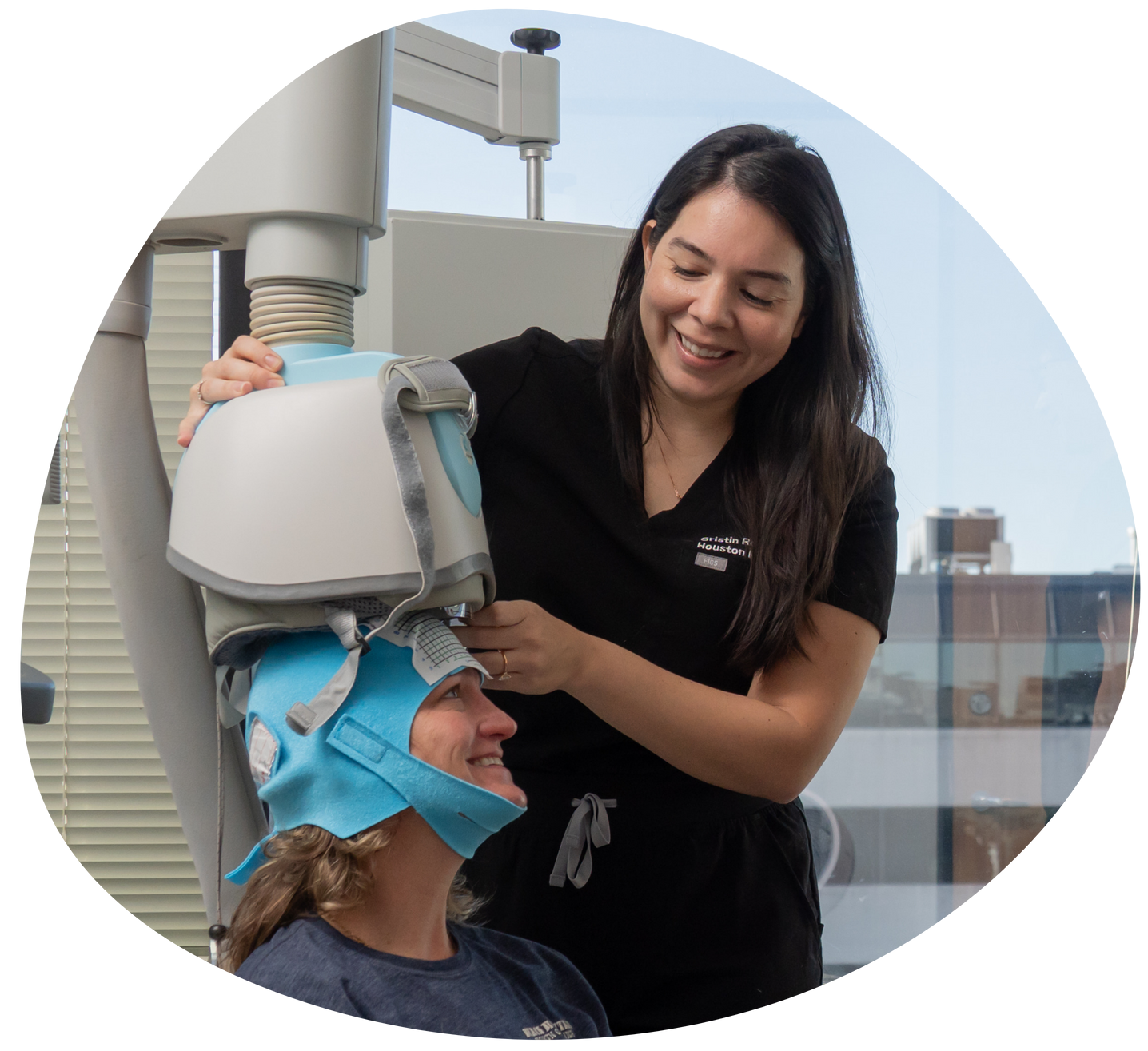 Clinician adjusting a blue head-mounted device on a seated patient in a medical setting
