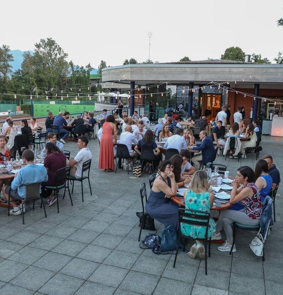 Ritrovo serale all'aperto con persone sedute ai tavoli, che socializzano e mangiano in un patio.