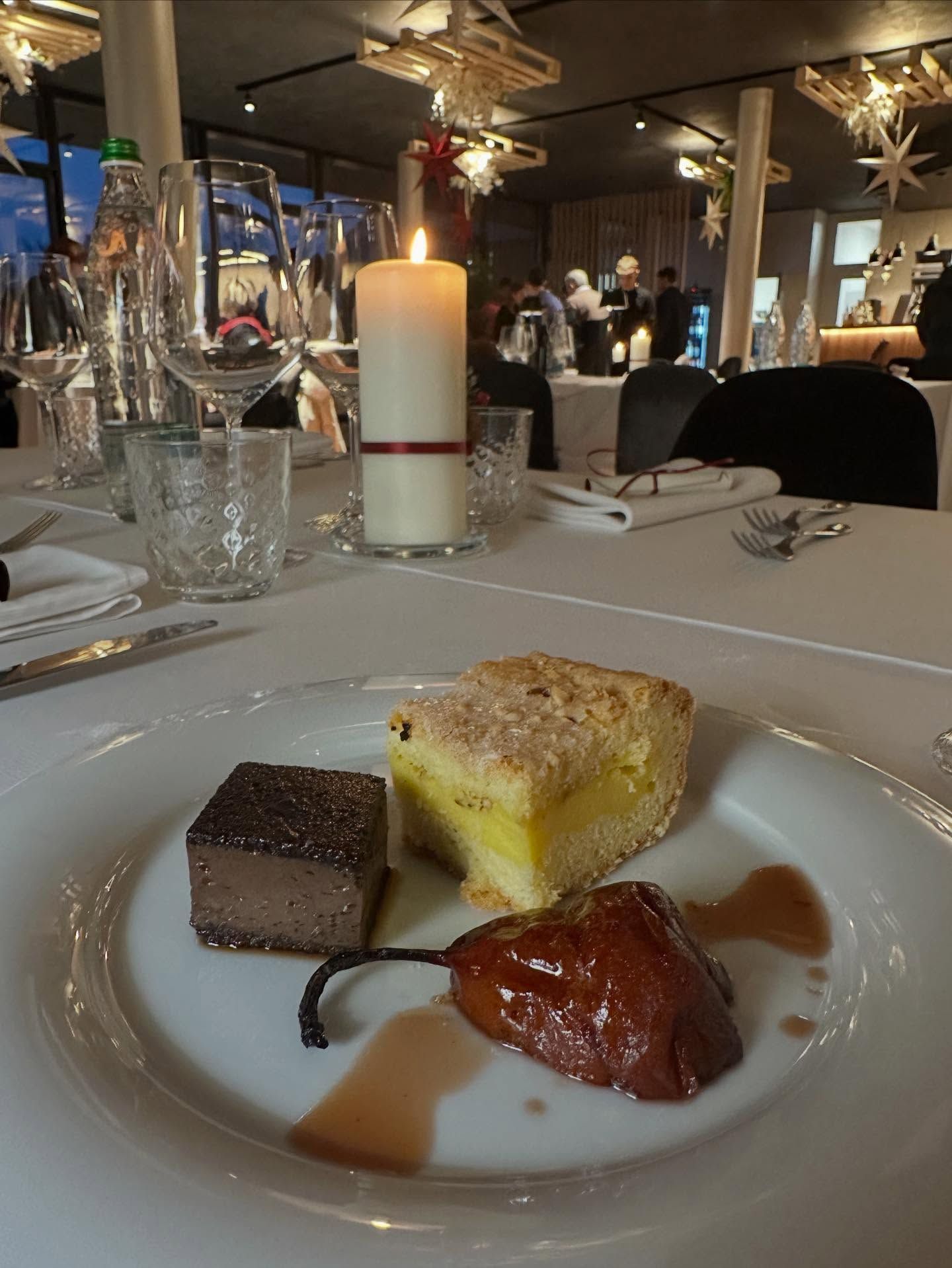 Piatto da dessert: quadrato di cioccolato, fetta di torta, pera caramellata, su un tavolo bianco in un ristorante.