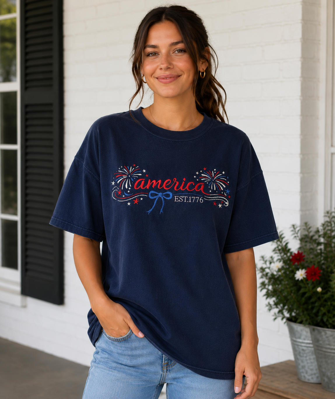 Woman standing on a porch wearing a navy graphic T-shirt and jeans, smiling at the camera.