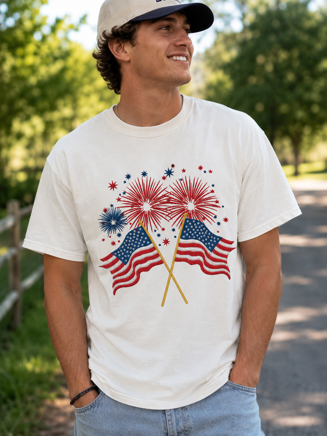 Man in white T-shirt with American flag and fireworks graphic, standing outdoors and smiling in a cap