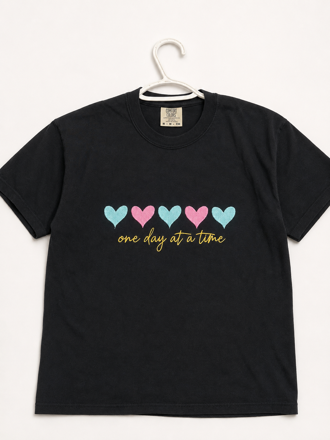 Woman standing in a black heart-print T-shirt and light blue jeans against a white background