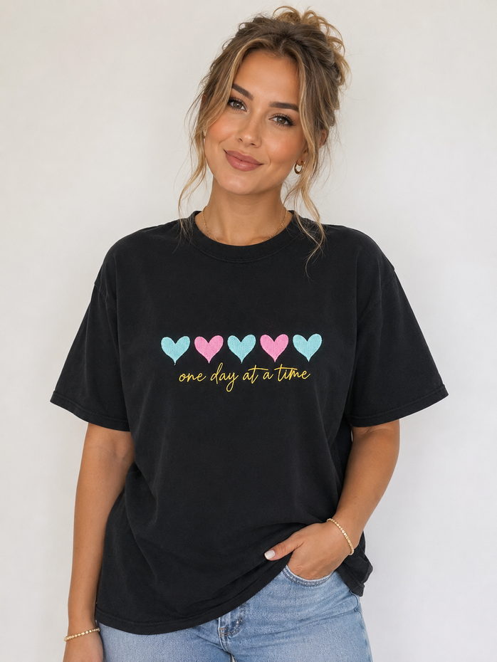 Woman standing in a black heart-print T-shirt and light blue jeans against a white background