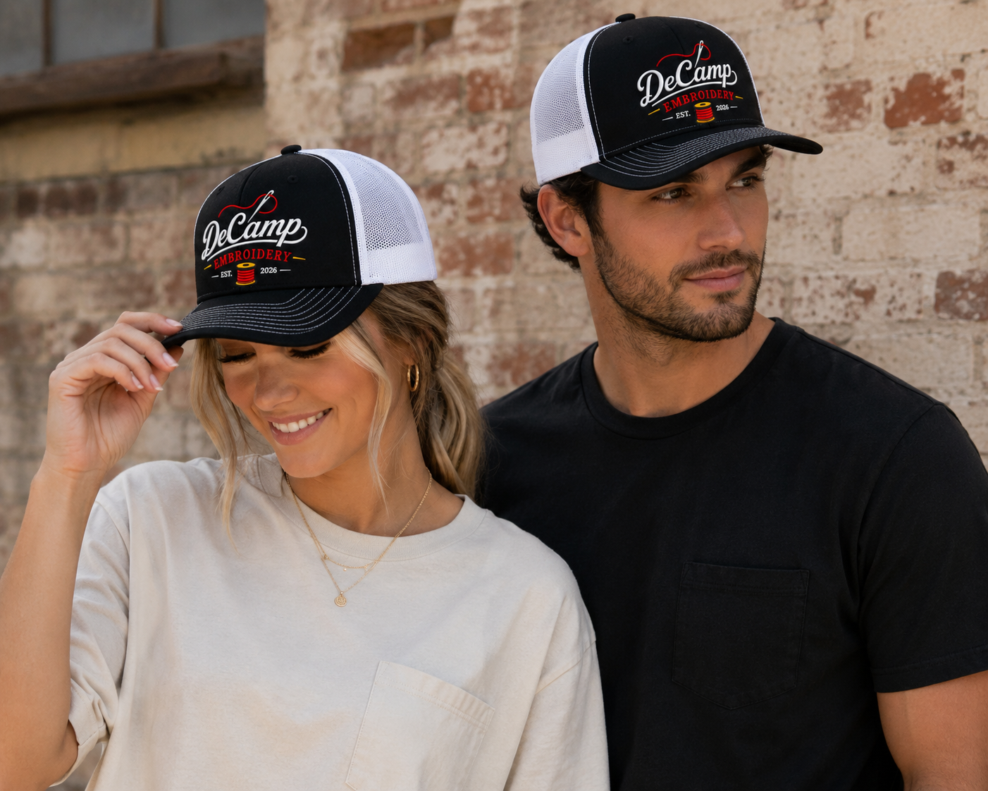 Two people in black-and-white caps, one adjusting her hat, standing against a brick wall