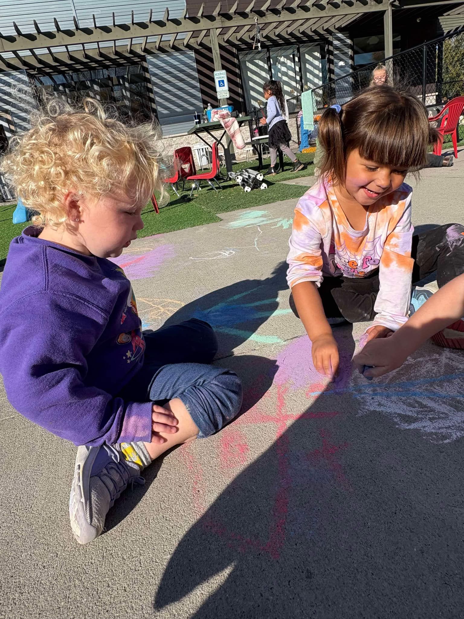 Two children drawing with chalk on a paved surface outside, creating colorful art.
