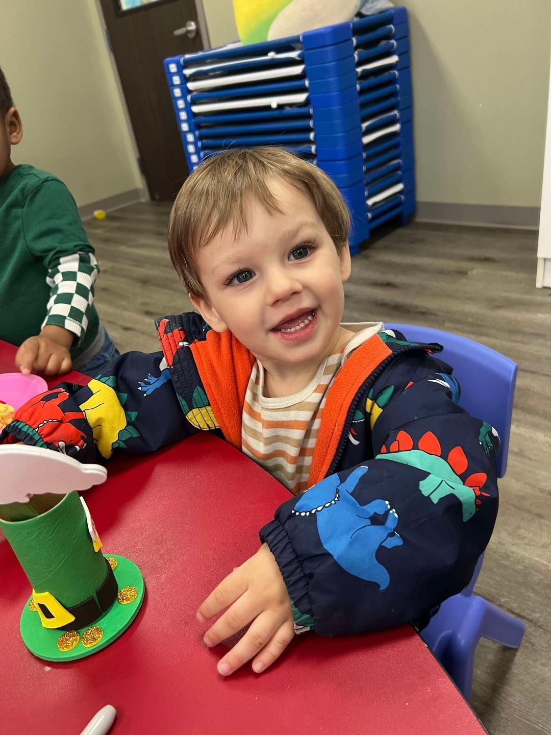Happy child in dinosaur jacket at a table, smiling.