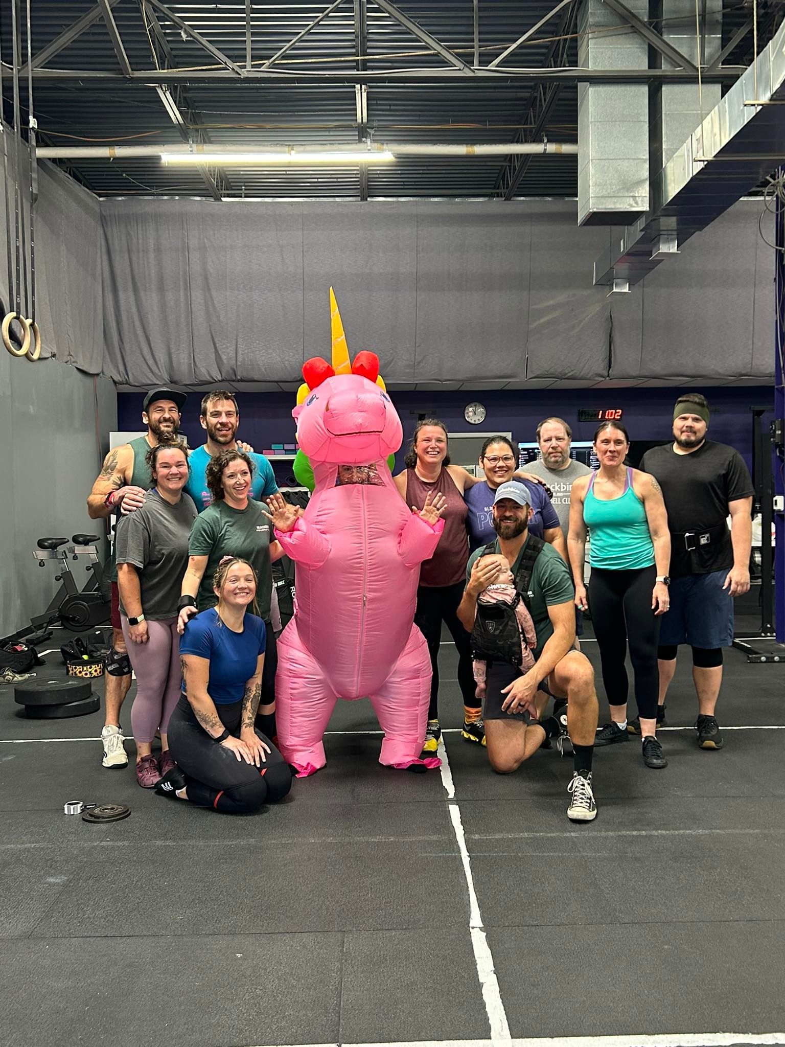 Group posing in a gym around a person in a pink unicorn costume