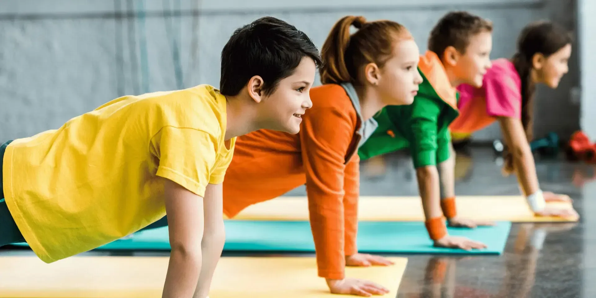 People doing plank exercises in a gym, each on a colored mat
