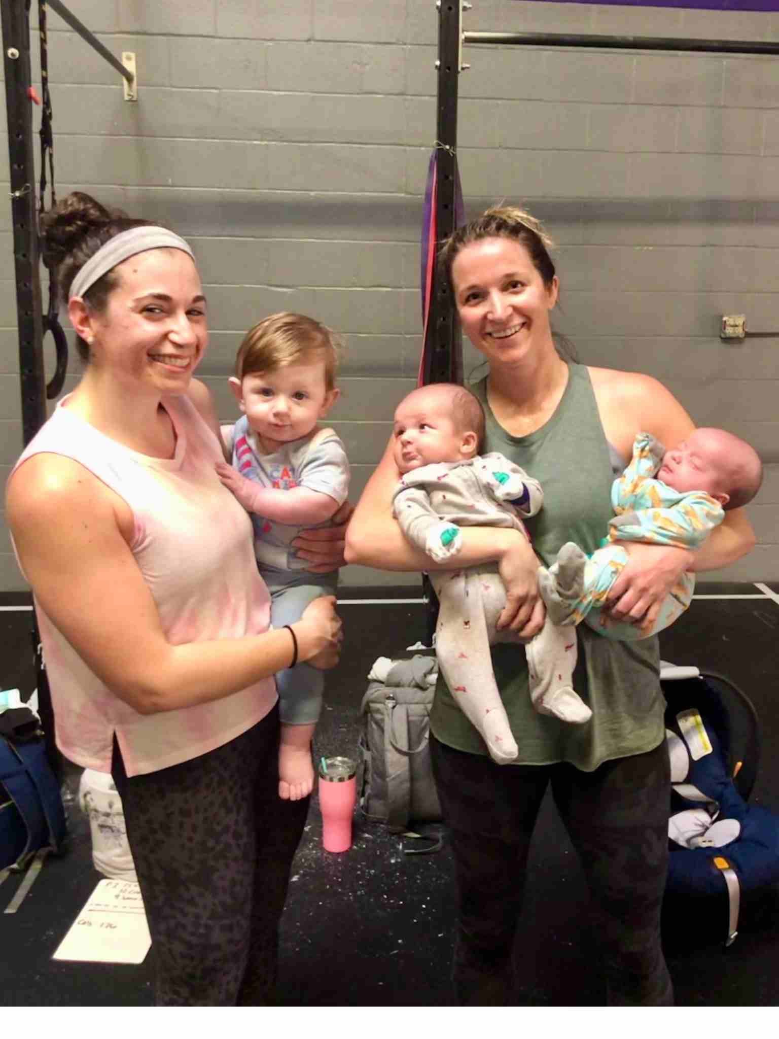 Two women are holding two babies in their arms in a gym.