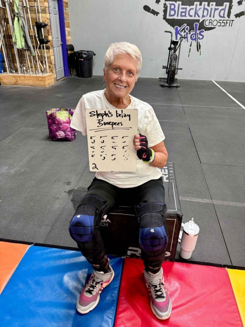 A woman is sitting on a bench in a gym holding a sign.