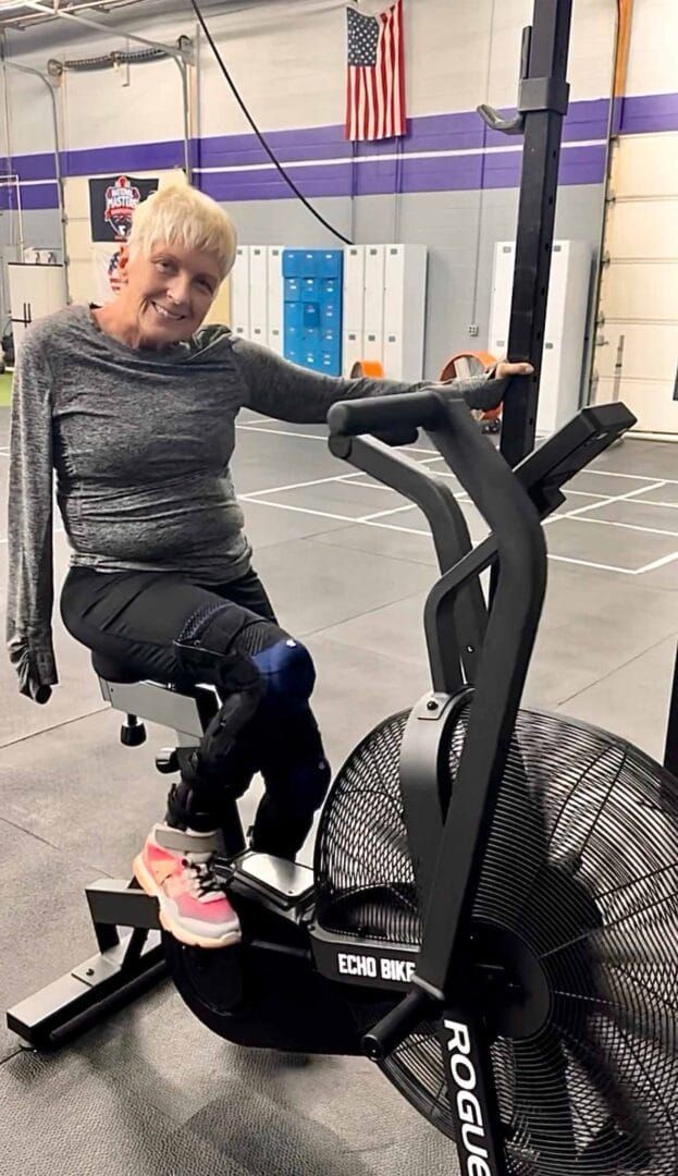 An elderly woman is riding an exercise bike in a gym.