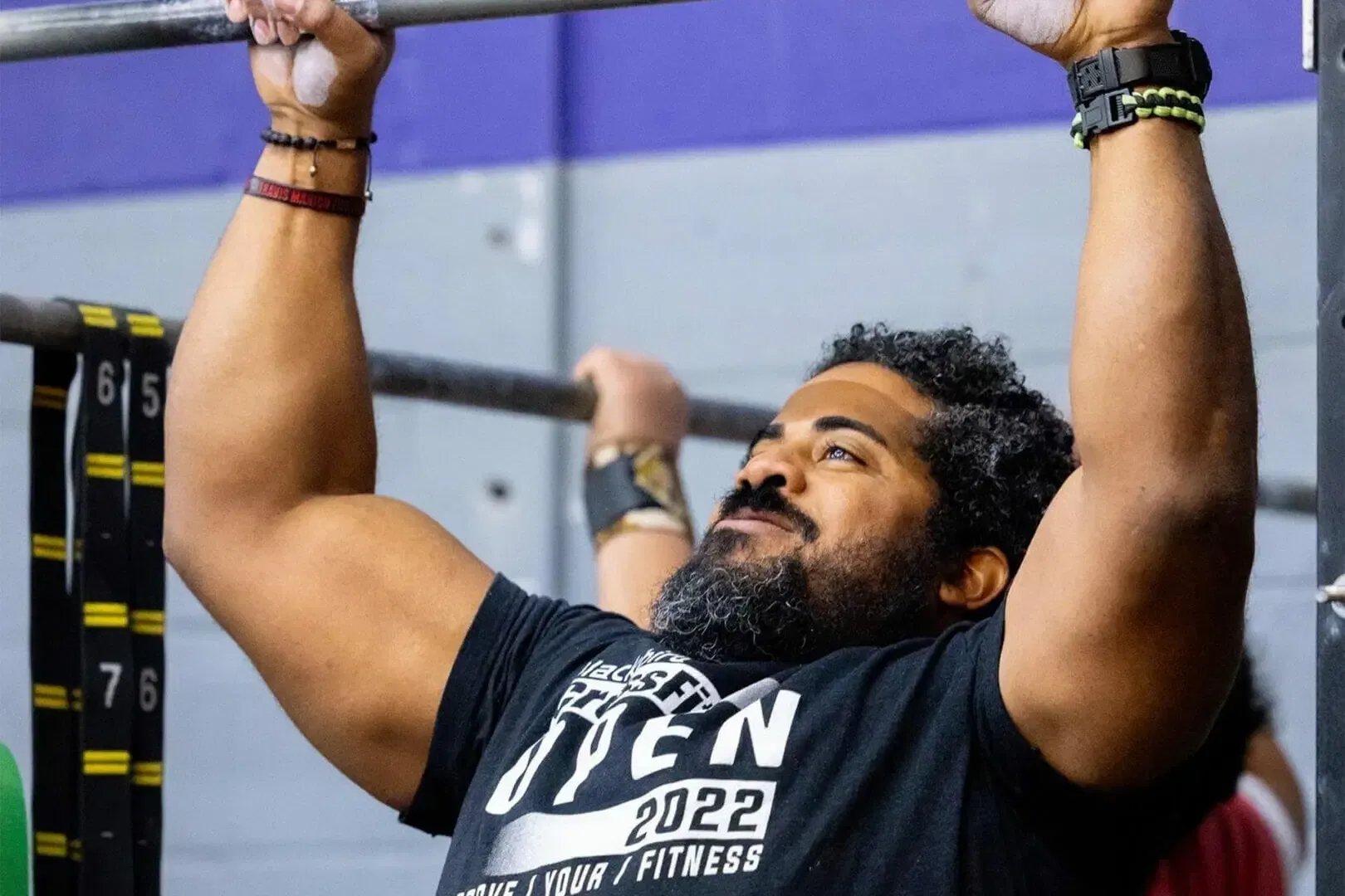 Man in black shirt doing a pull-up in a gym, with arms raised and focused expression