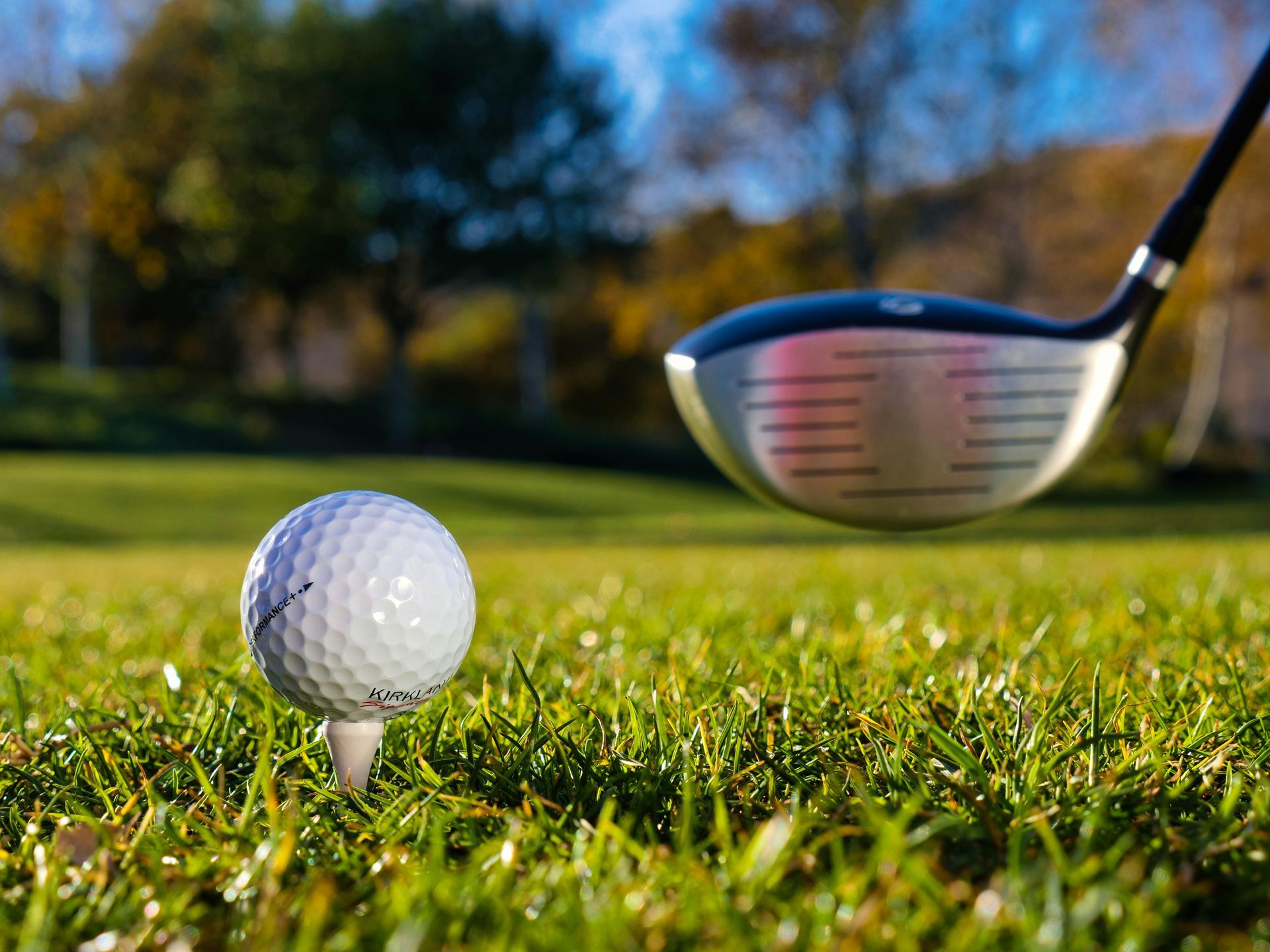 Golf ball on tee with a club about to swing in green grass.