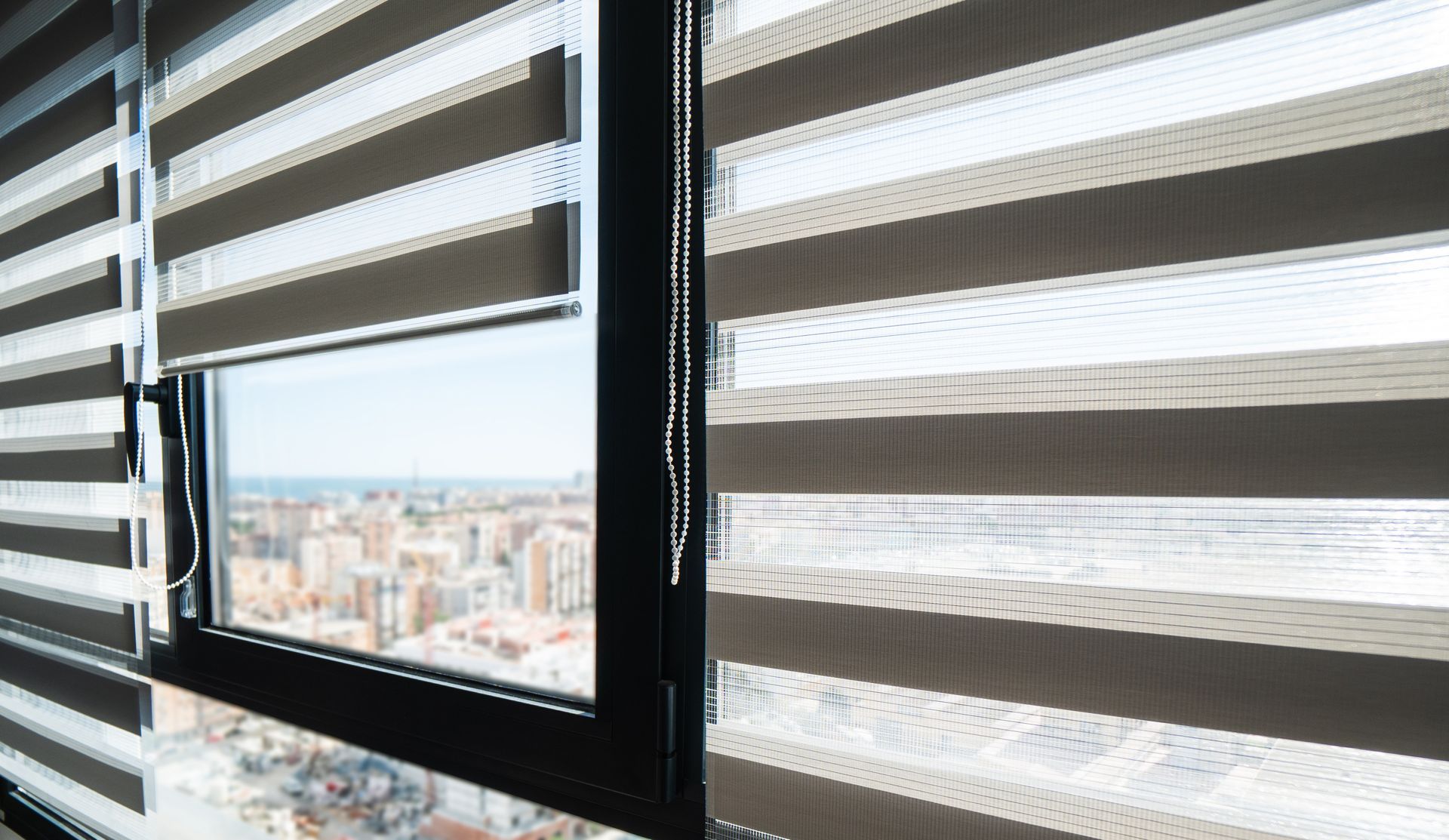 Modern zebra blinds on a window overlooking a blurred city skyline.