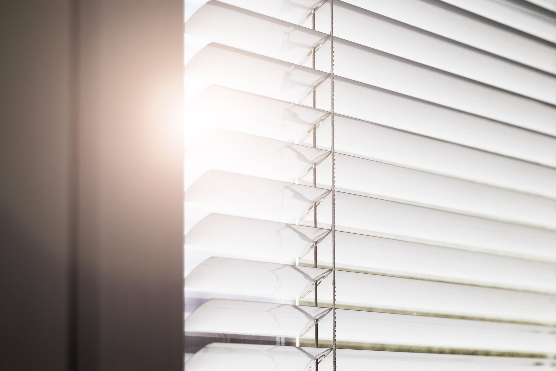 The sun is shining through the blinds of a window.