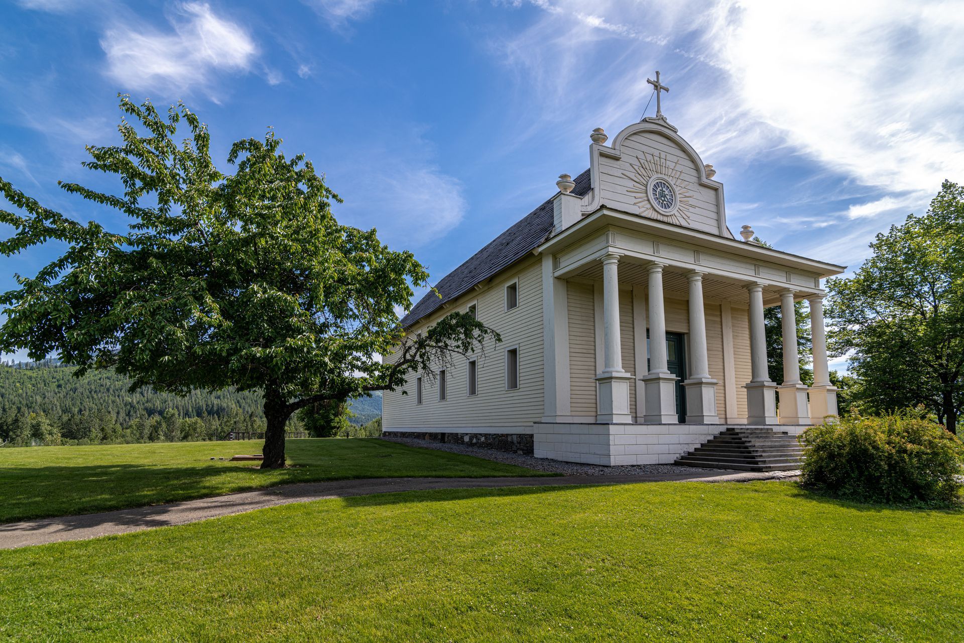 a small white building with columns and a cross on top of it is sitting in the middle of a grassy field .