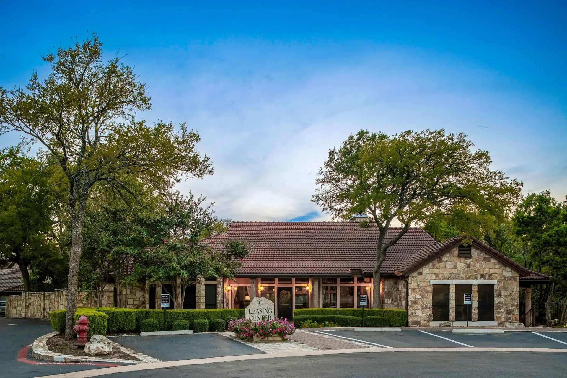 Exterior of a stone building with a tiled roof, marked as 'Leasing Center', surrounded by trees and landscaping.
