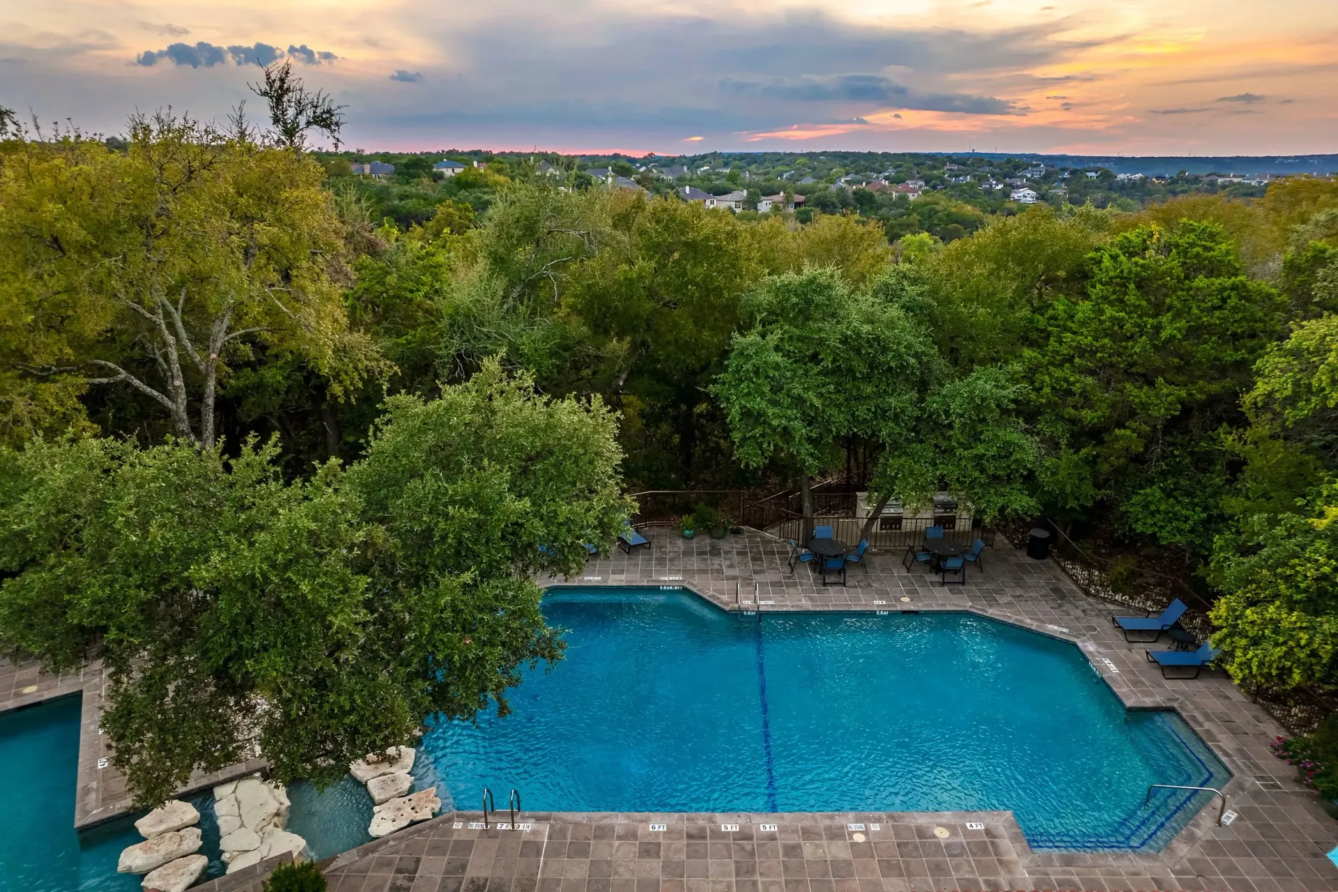 Aerial view of a resort-style swimming pool and patio area surrounded by lush trees.