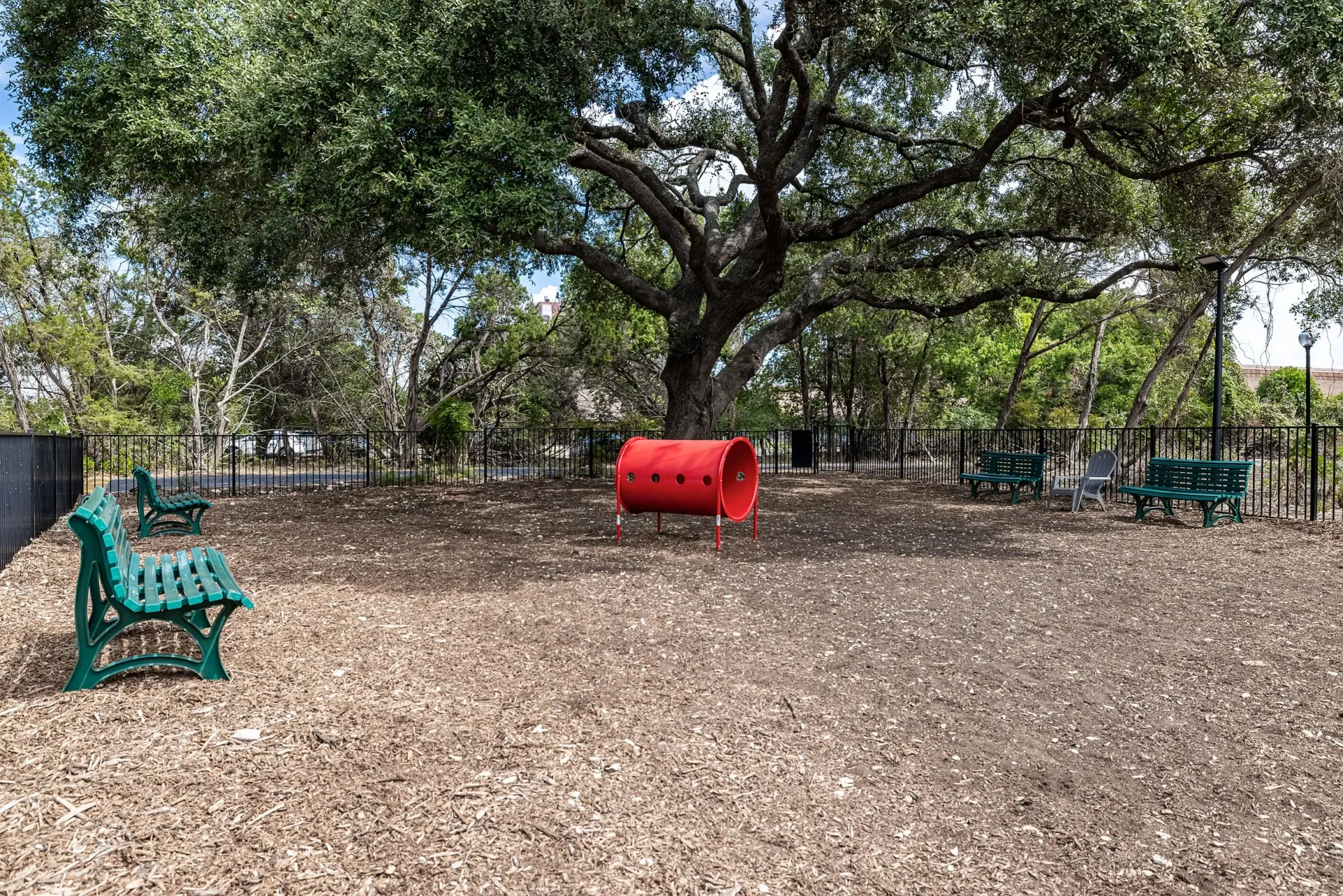 Outdoor dog park with benches and a red agility tunnel.