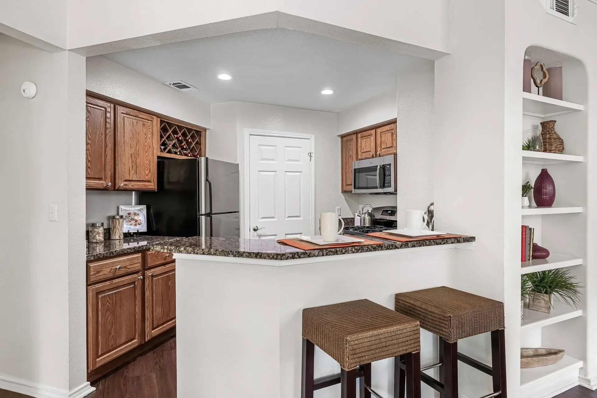 Kitchen with granite countertops, wood cabinets, stainless steel refrigerator, and a breakfast bar with stools.