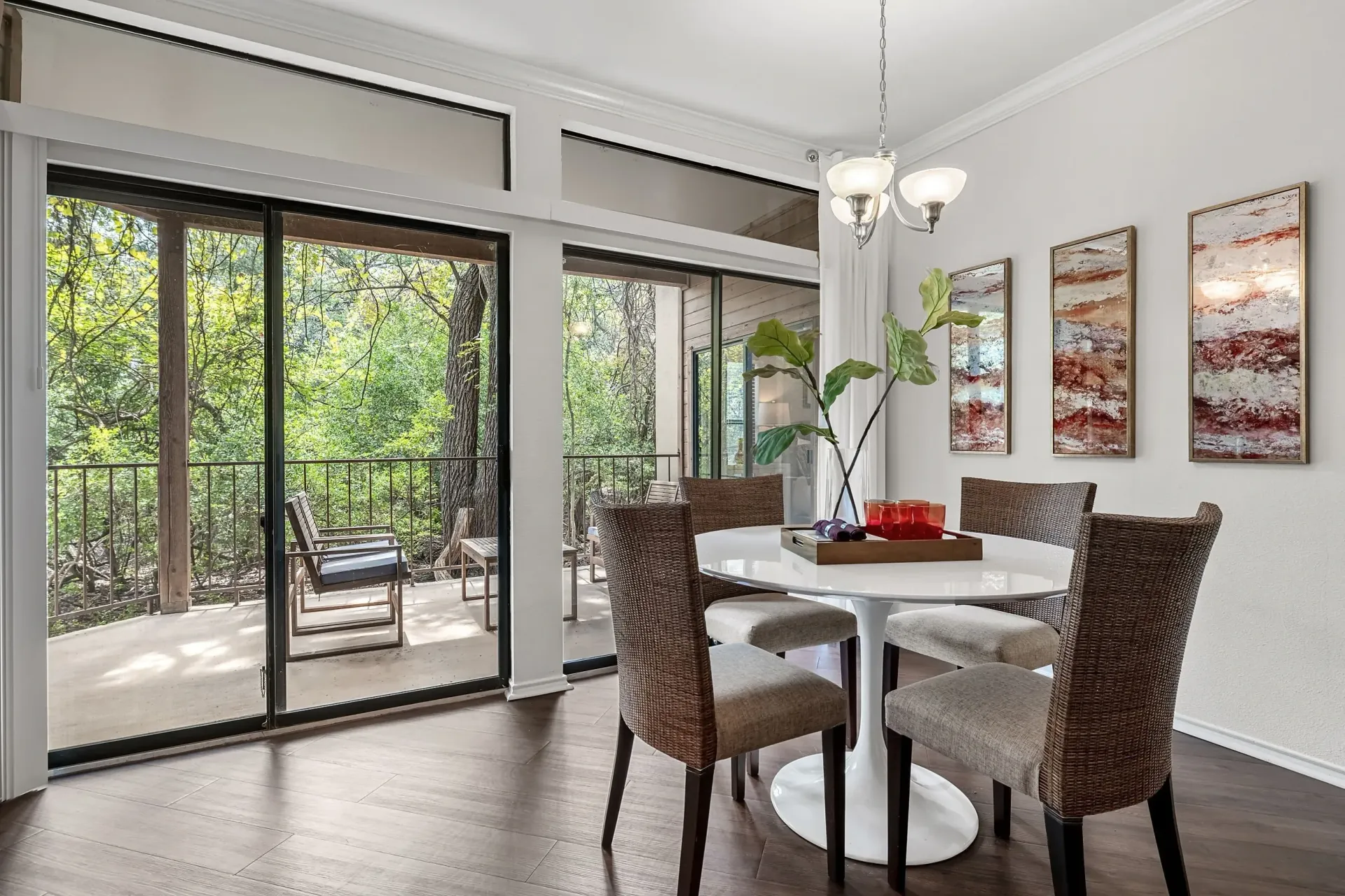 Dining area with a white table and chairs, overlooking a balcony with trees.
