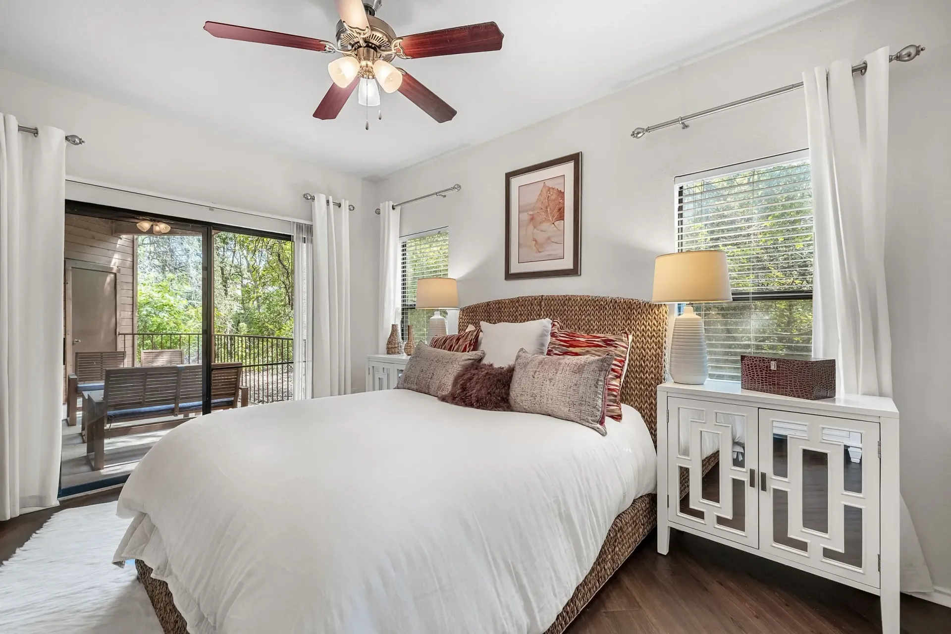 Bedroom with a king-size bed, white bedding, and patio access. Features a ceiling fan and two bedside tables with lamps.
