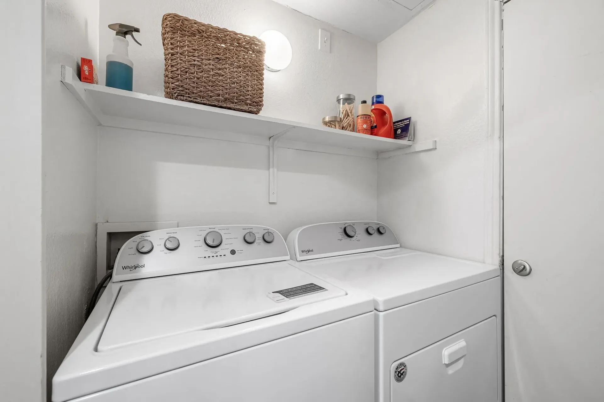 Washer and dryer set with a shelf above containing cleaning supplies.