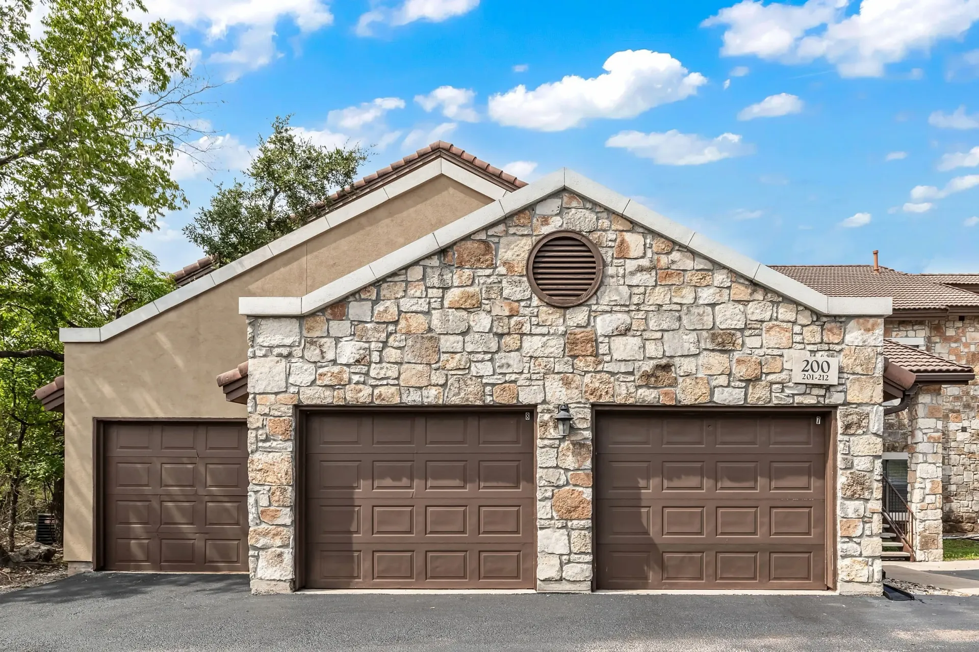 Three garage doors on a stone building with a Spanish tile roof and blue sky.