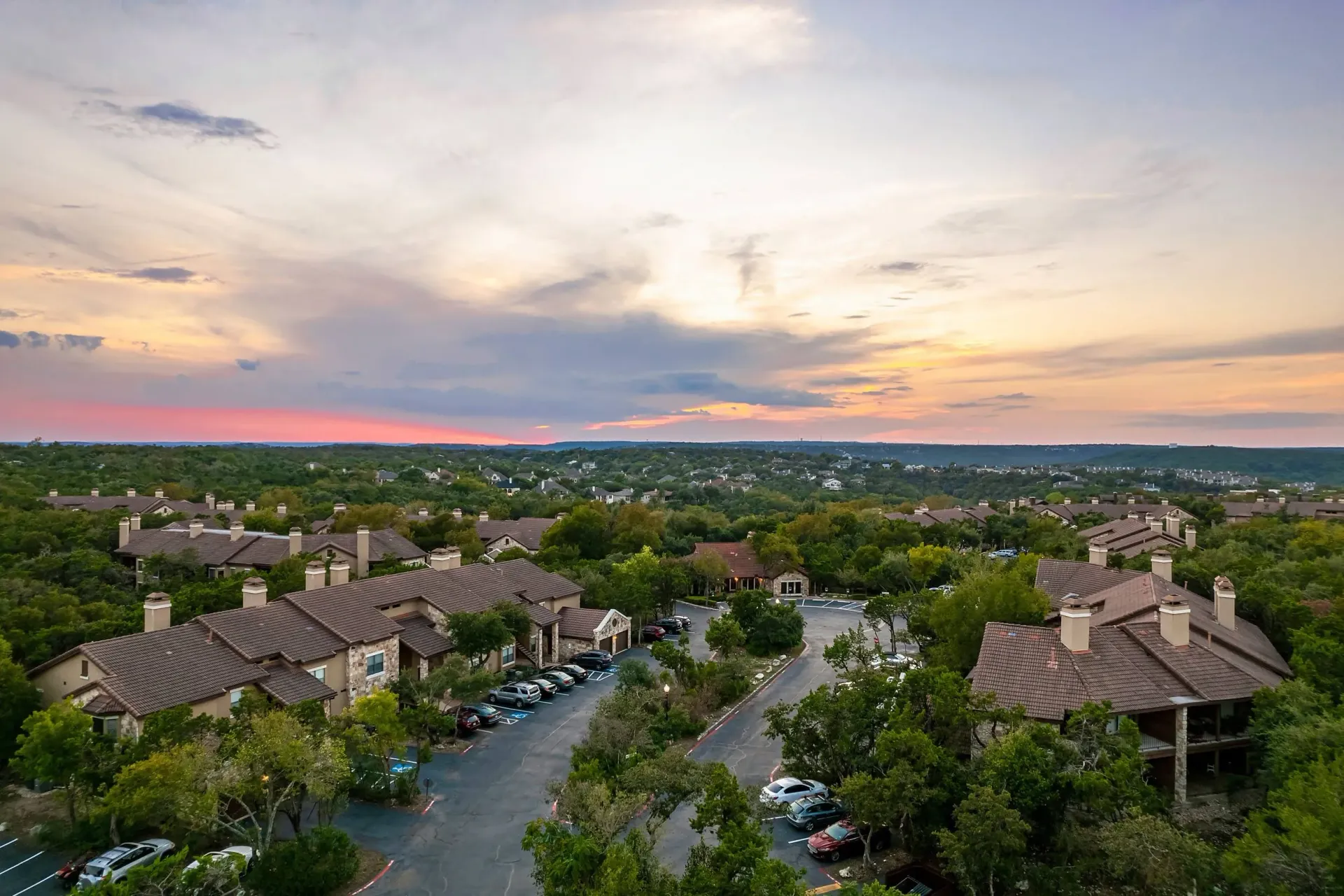 Aerial view of apartment buildings nestled among lush trees at sunset.