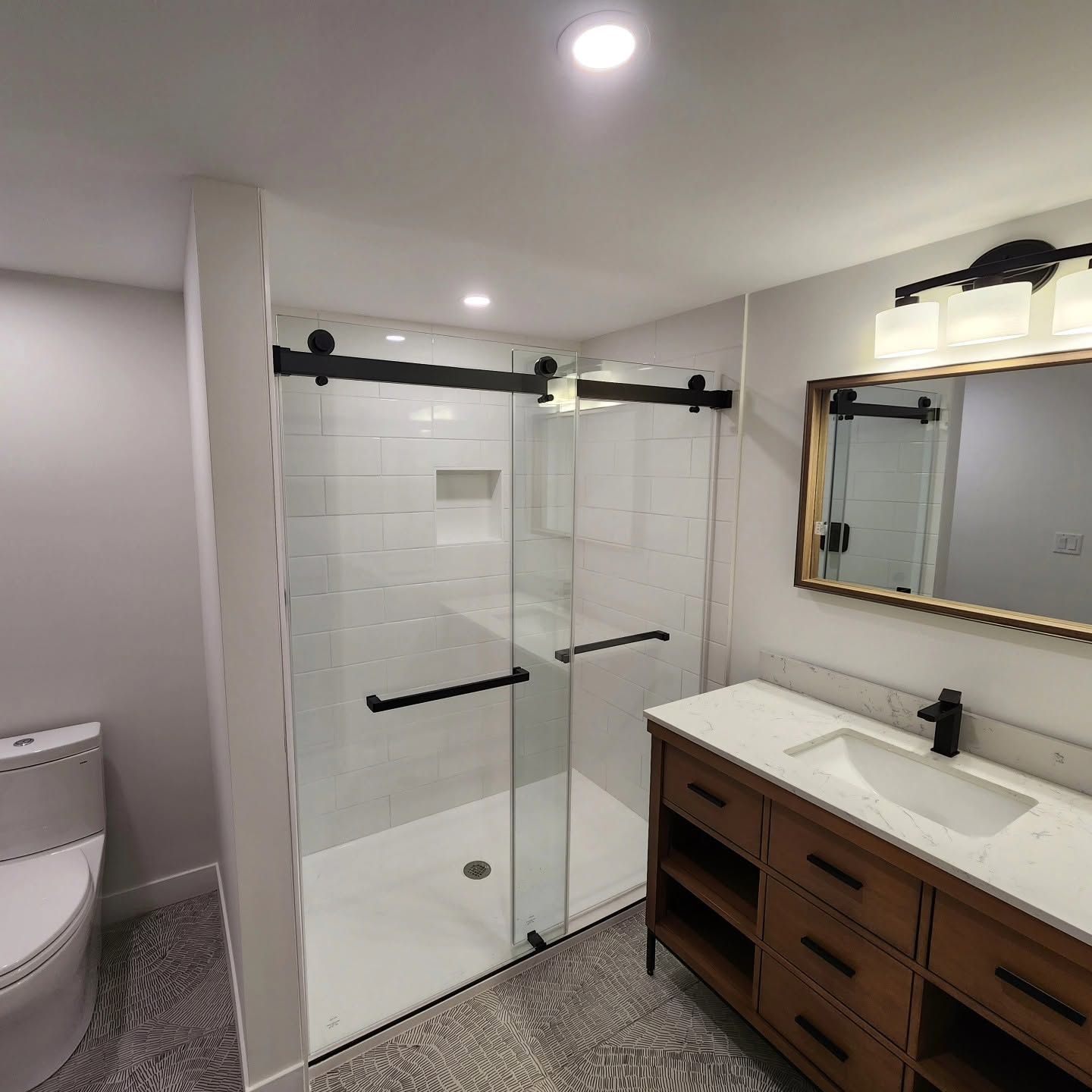 Modern bathroom with glass shower, white tile, vanity with wood drawers, and mirror.