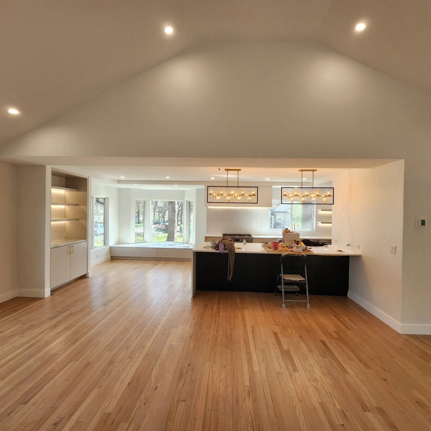 Spacious open-concept living room with hardwood floors, vaulted ceiling, and a kitchen island under pendant lights.