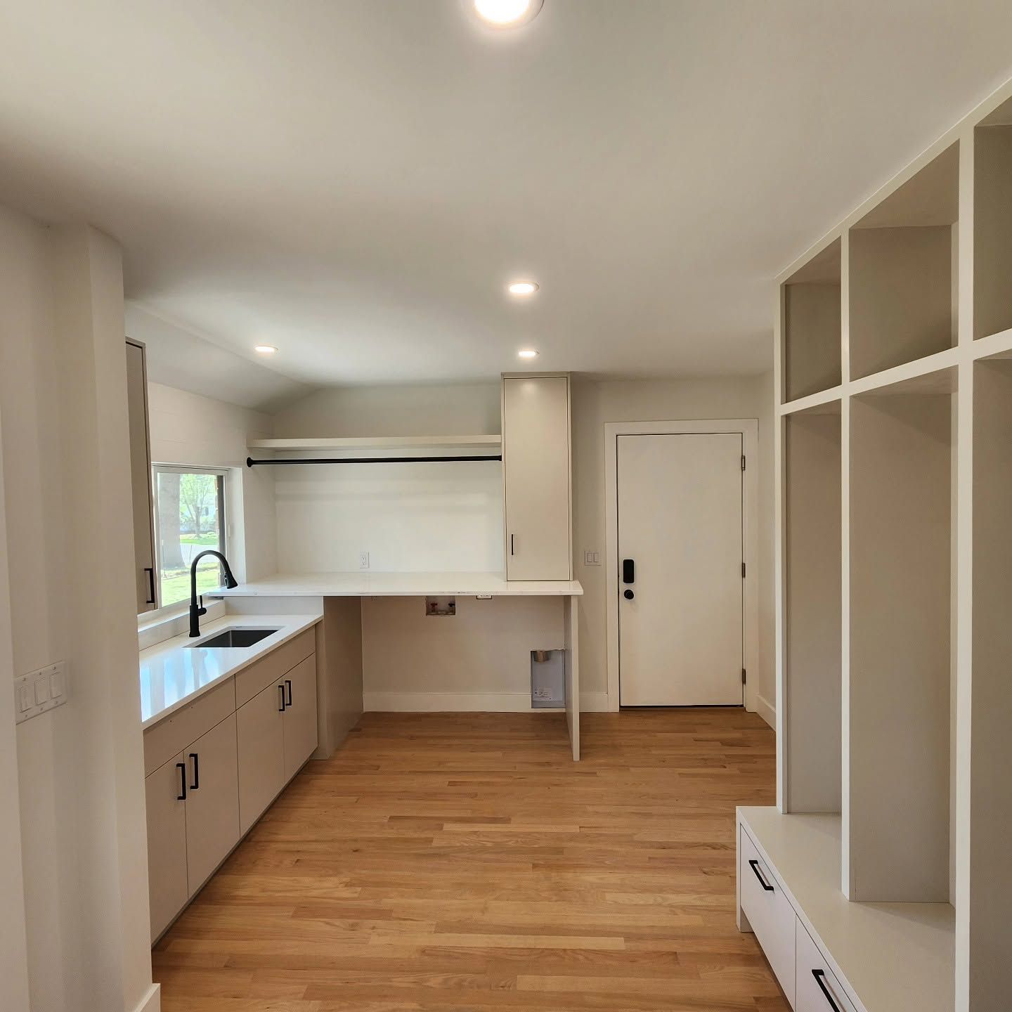 Empty modern kitchen with white cabinets, wood flooring, built-in shelves, and a door at the back